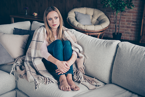 Woman sat on a sofa with a blanket covering her